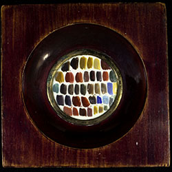 Small swatches of different colored paint on white background placed within round opening of square wooden frame